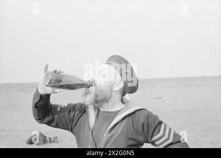 WITH A DESTROYER FLOTILLA AT SEA. AUGUST 1940, ON BOARD SHIPS OF THE FLOTILLA. - A bearded sailor enjoys a drink from a bottle during an impromptu football match ashore Stock Photo