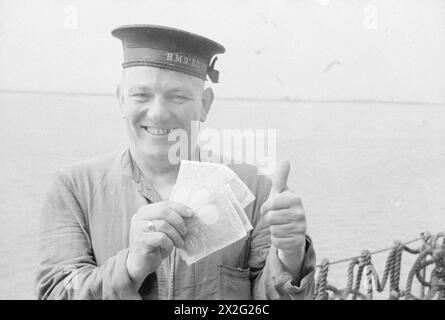 WITH A DESTROYER FLOTILLA AT SEA. AUGUST 1940, ON BOARD SHIPS OF THE FLOTILLA. - Ship's Pay. A happy sailor on board HMS KELVIN holds up a handful of notes for all the world to see Stock Photo