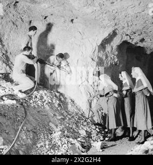 IN A GIBRALTER UNDERGROUND HOSPITAL - When most of the civilian population of Gibralter was evacuated, a hospital was established in one of the air raid shelters cut into the solid rock. It is constantly being added to and is ready for any eventuality. The work of excavation is being done by Civilian engineers, leaving the Royal Engineers to concentrate on defence works. This image shows skilled civilian workmen of the new City Council's staff engaged in construction of a new ward of the hospital. Officer Commanding Hospital and Nursing Staff look on British Army, Royal Engineers Stock Photo