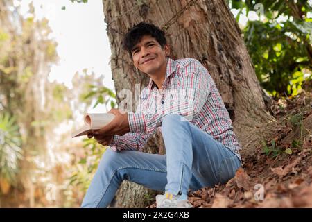 Lifestyle. young latin man sitting under a tree reading a book Stock Photo