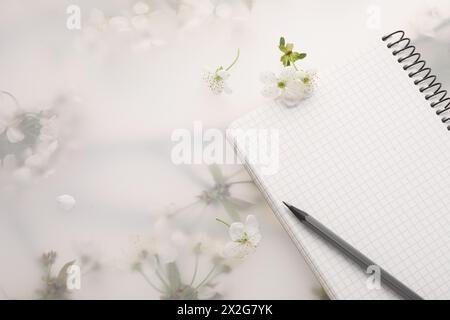 Guest list. Notebook, pencil and beautiful cherry tree blossoms on spring floral background, flat lay. Space for text Stock Photo