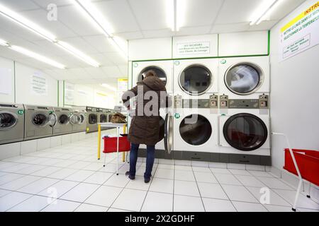 woman put laundry in washing machine in empty public laundry Stock Photo
