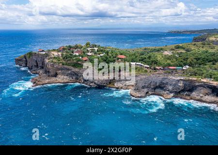 An aerial shot shows a cliff by the azure ocean, blending with the sky and clouds. The natural coastal landscape features vegetation on the rocky terr Stock Photo