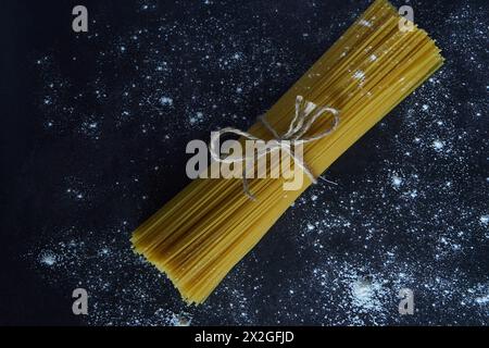 Uncooked spaghetti tied with a rustic cordon on a black background sprinkled with flour Stock Photo