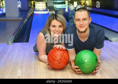 Girl and man lie on parquet in club and hold balls for bowling, focus on woman Stock Photo