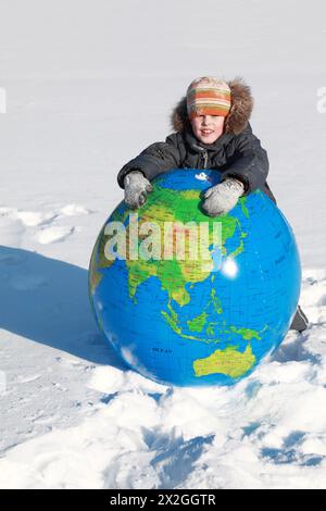 little boy leans on large inflatable globe on outdoors in winter Stock Photo