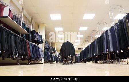few rows of jackets and men trousers on hangers in big light shop; school clothing Stock Photo
