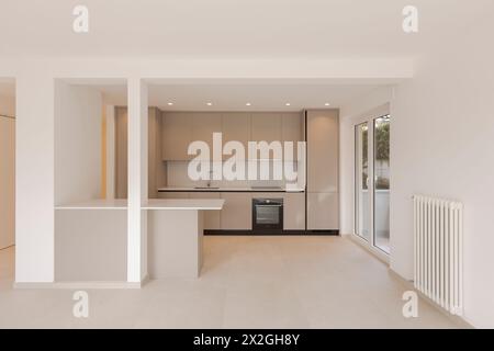 Interior of a modern beige kitchen, with a work table in front. The ceiling is white, and to the right is a large window. Stock Photo