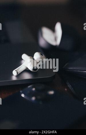 A pair of sleek, white, wireless earphones rest on a silver laptop with a black keyboard. The earphones are designed for comfort and style. Stock Photo