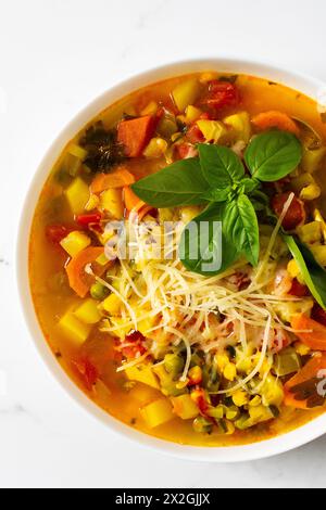 Minestrone soup from zucchini and tomato, onion and carrots, corn and peas with parsley, bowl of soup garnished with parmesan and basil close-up, vegetarian soup Stock Photo