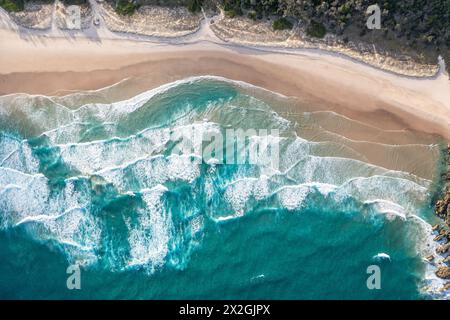 Foamy ocean waves roll and approach sandy beach. Majesty turquoise seascape. Top view from drone. Stock Photo