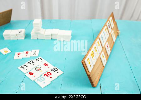 Plastic tiles from the game rummikub, rummicub or  okey in Turkey arranged on a wooden rack, on blue table Stock Photo