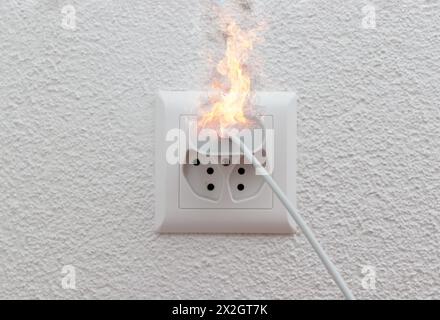 Socket or wire plug malfunction burning phone charger in indoor, electric short circuit causing fire on plug socket Stock Photo