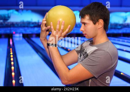 Young man holds yellow ball and prepares to throw in bowling; profile of man Stock Photo