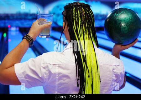 Back of man, which holds ball and cocktail and prepares to throw in bowling club Stock Photo