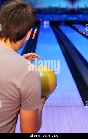 Back of young man, which holds yellow ball and prepares to throw in bowling club; focus on ball Stock Photo