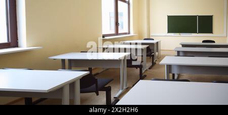 Empty beige classroom with wooden school desks and simple black chairs, view from desk on school board Stock Photo