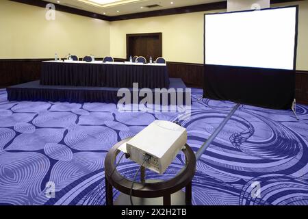 Big table with microphone near screen in bright conference hall, view from projector Stock Photo