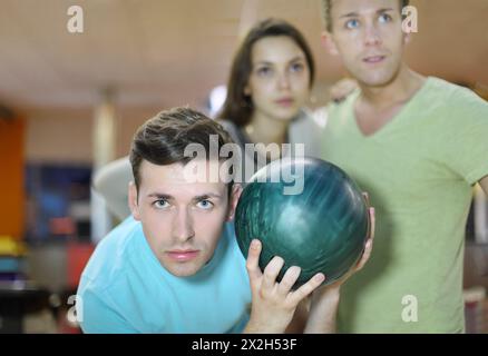 Young man prepares to throw of green ball in bowling; man and woman look away; focus on left man; shallow depth of field Stock Photo