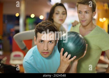 Young man prepares to throw of ball in bowling; man and woman look at him; focus on left man; shallow depth of field Stock Photo