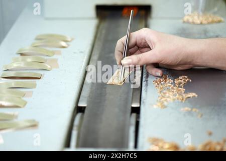 Female hand with tweezers, gold items on the conveyer belt, focus on pointer finger Stock Photo