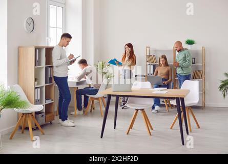 Group of young business people men and women in casual clothes talking on their workplace. Stock Photo