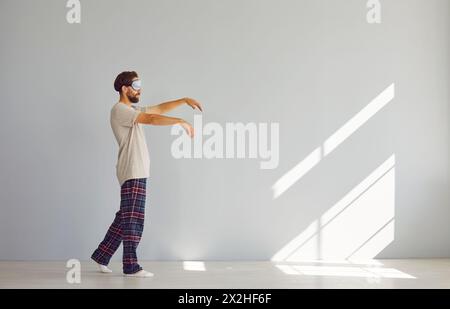 Full length portrait of young sleepwalker man in pajamas suffering from sleepwalking in sleep mask Stock Photo