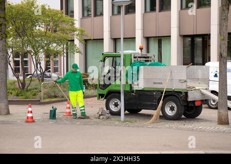Basel, Switzerland - April 18, 2024: Young man in green uniform, from city gardening service,  working with shovel on repairing sidewalk cobblestone Stock Photo