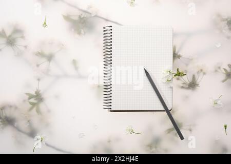 Guest list. Notebook, pencil and beautiful cherry tree blossoms on spring floral background, flat lay. Space for text Stock Photo