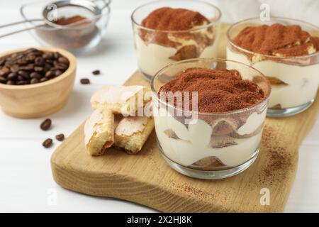 Delicious tiramisu in glasses, cookies and coffee beans on white table, closeup Stock Photo