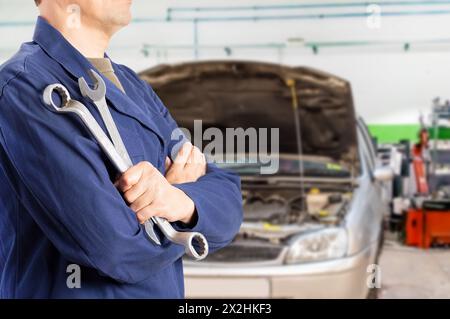 Cropped image of a male mechanic standing while holding two wrenches in a car mechanic shop Stock Photo