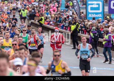 Mass of club runners and fun runners competing in the TCS London Marathon 2024 passing through Tower Hill, London, UK. Runner Hugo Fry in Santa suit Stock Photo