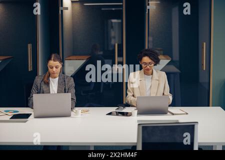 Concentrated female office workers working on project and use laptops sitting in coworking Stock Photo