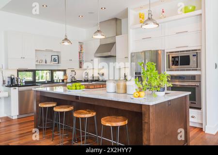 Kitchen area with white cabinets, marble top wooden island with painted black steel and exotic wood barstools, black granite countertops inside a Stock Photo