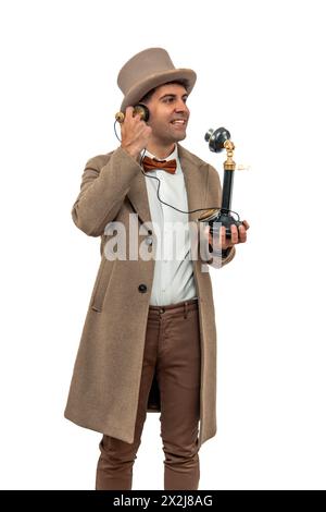 vertical, early 20th century vintage gentleman sporting a bowler hat and trench coat, as he makes a call using an antique English telephone. Experienc Stock Photo