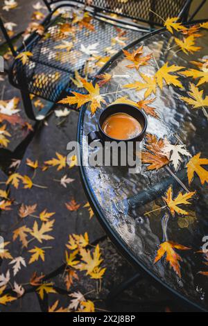 Cup of coffee standing on the patio table after the fall rain with lots of fallen maple yellow leaves Stock Photo