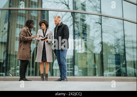 Three business colleagues laughing and discussing work outdoors, reflecting teamwork, diversity, and professional engagement. Stock Photo