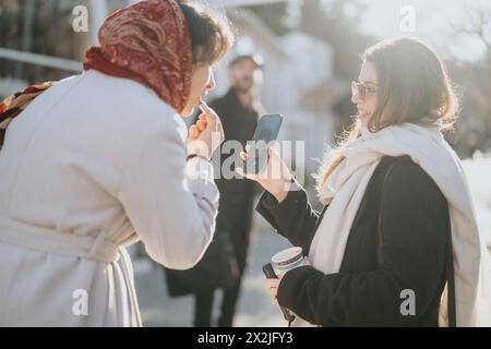 Two young businesswomen using smart phone to strategize and discuss trends during an outdoor meeting in a bustling urban setting. Stock Photo