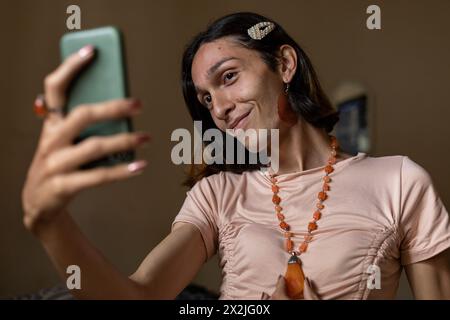 A young transgender man (22) is in his room smiling while taking a self-portrait using his smartphone. Concept of transgender and communication Stock Photo