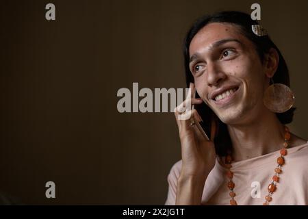 A young transgender man (22) is in his room talking on his smartphone while smiling. Concept of transgender and communication Stock Photo