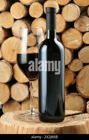 Stylish presentation of red wine in bottle and wineglass near wooden logs Stock Photo