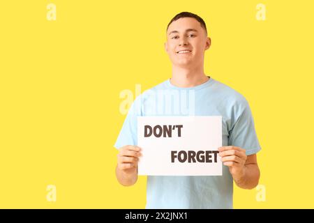 Young man holding paper with text DON'T FORGET on yellow background Stock Photo