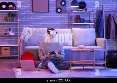 Male student in VR glasses playing video game at home in evening Stock Photo