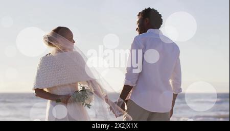 Image of light spots over african american couple getting married on beach Stock Photo