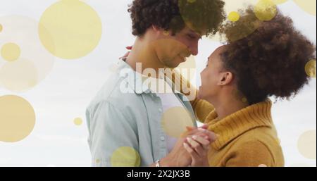 Image of light spots over happy biracial couple dancing on beach Stock Photo