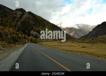A new asphalt road crosses a valley with a crevice in the mountains on a cloudy autumn day. Chuisky tract, Altai, Siberia, Russia. Stock Photo