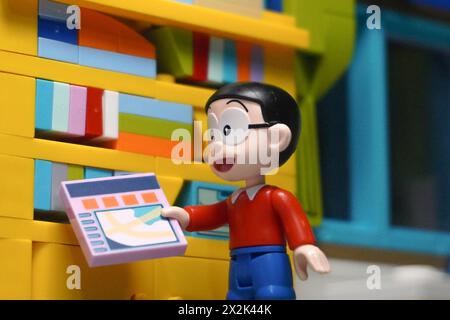 Japanese toy figures (Nobita and Doraemon) are standing near a bookshelf holding a book Stock Photo