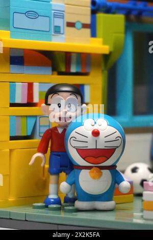 Japanese toy figures (Nobita and Doraemon) are standing near the bookshelf with a smile Stock Photo