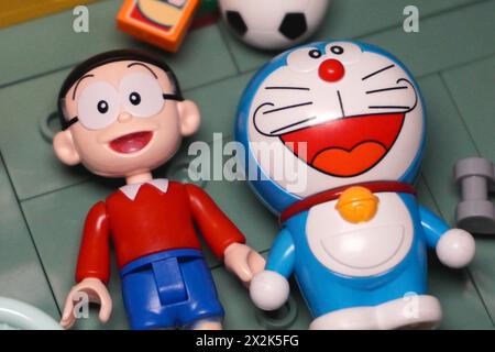 Japanese toy figures, namely Nobita and Doraemon, are lying together on the floor, smiling among the objects Stock Photo