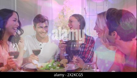 Image of bokeh over happy caucasian female and male friends drinking wine and talking Stock Photo